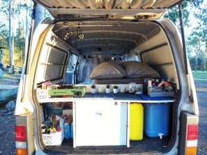 Arrière d'un van aménagé : cooker, bidons d'eau et d'essence, ustensiles de cuisines