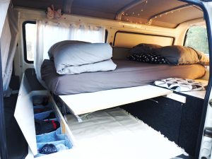 Chambre d'un van aménagé : matelas, couette, oreiller et rangements